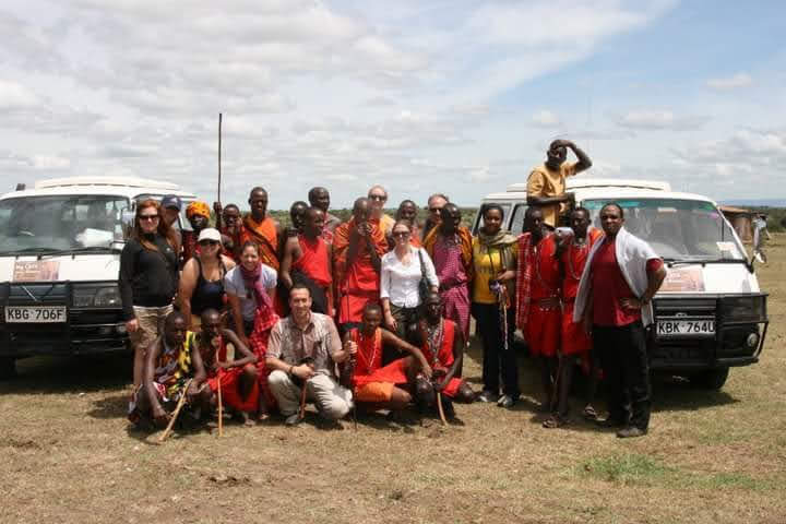 Big Cats Africa Safari team posing with tour vans in Kenya. The team is composed of local guides and international tourists, showcasing the company's expertise in providing personalized safari tours and travel services.